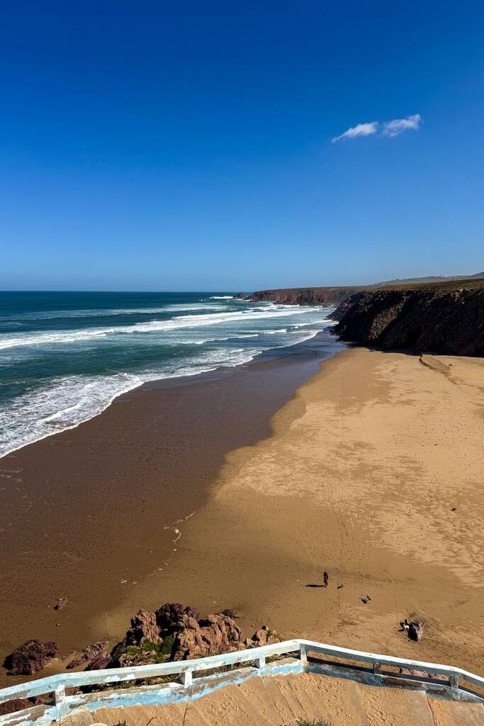 Breathtaking clifftop perspective of Mirleft Beach with vibrant waves and clear skies in Morocco.